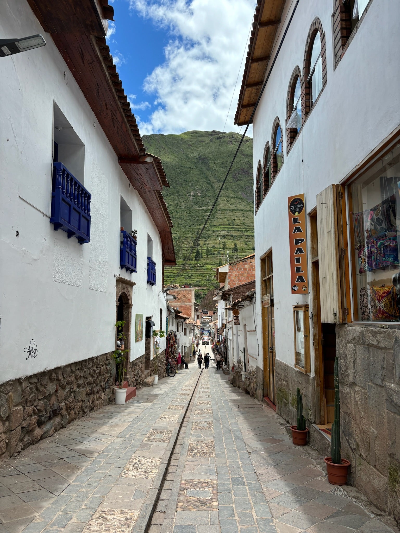 Tiled street in a mountainous area with white buildings and blue shutters.